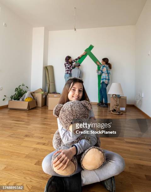 teenagers are hanging out in a new apartment, a little girl sits in front and holding happily at a teddy bear - bear on white stockfoto's en -beelden