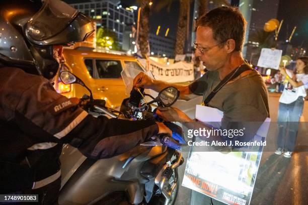 Demonstrator ties a yellow ribbon, which is being used to support the releasing of hostages captured by Hamas, onto a person's motorcycle in rally...