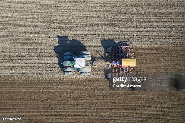 Aerial view over tractor with pneumatic seed drill, agricultural machine for sowing, working on a field in spring.