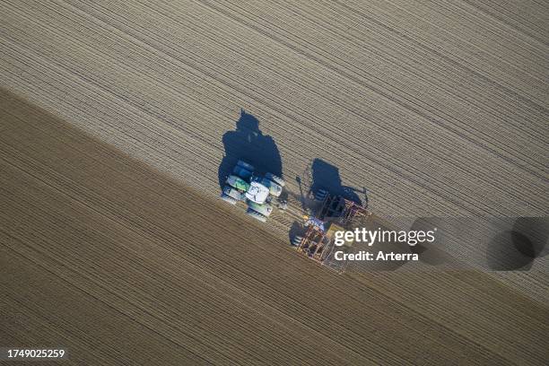 Aerial view over tractor with pneumatic seed drill, agricultural machine for sowing, working on a field in spring.