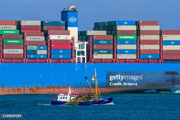 Little fishing boat passing huge Chinese COSCO Shipping container ship loaded with containers on the North Sea, sailing under flag of Hong Kong,...