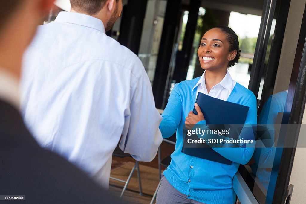 Friendly businesswoman shaking hands and greeting client in office doorway