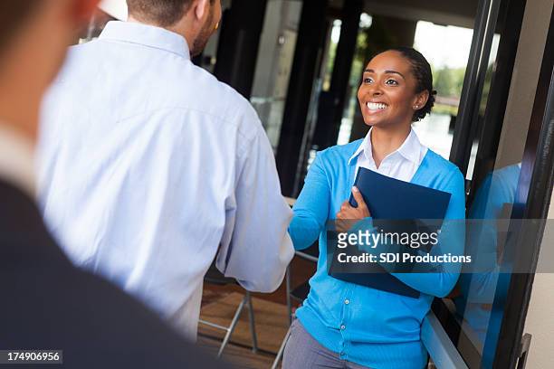 friendly businesswoman shaking hands and greeting client in office doorway - temptation stock pictures, royalty-free photos & images