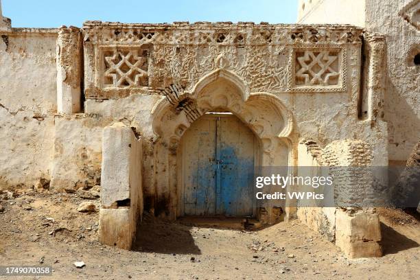 Badly decaying building features a facade decorated with star and floral motifs, its mud brick showing through the whitewashed plaster facade,...