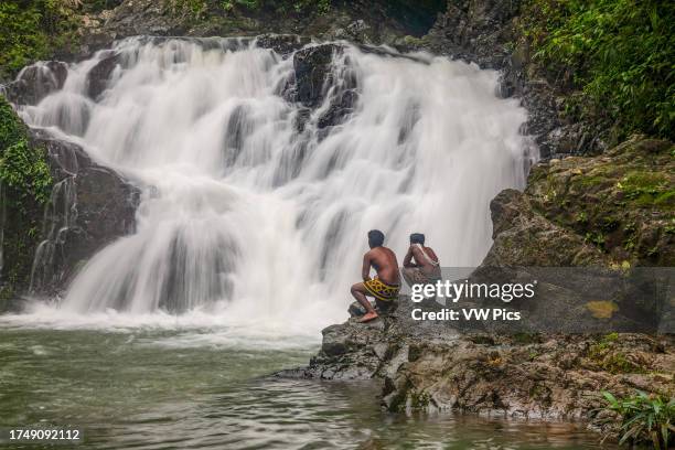 Two young indigenous Embera men in traditional dress stand by a waterfall on the Chagres River in Panama.