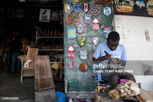 An artisan works on a carving in front of a display of wooden art depicting logos of popular european soccer clubs that are a popular souvenir with...