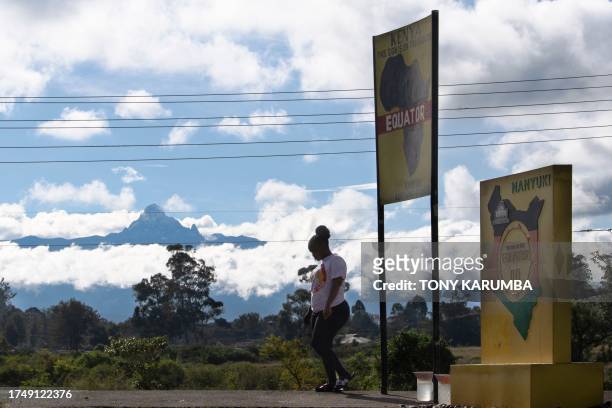 Resident of Nanyuki town walks past markers indicating the point of the equator crossing while the peaks of Kenya's highest mountain, Mt. Kenya,...