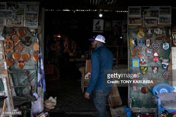 An artisan stands in the doorway of a tourist shop displaying at its entrance wooden art depicting logos of popular european soccer clubs and varied...