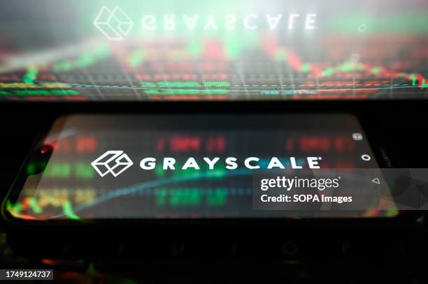 In this photo illustration, Grayscale logo is displayed on a smartphone with stock market percentages reflections.