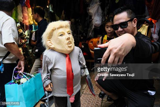 Man takes a selfie with a doll wearing Donald Trump mask in a market selling Halloween accessories on October 28, 2023 in Hong Kong, China.