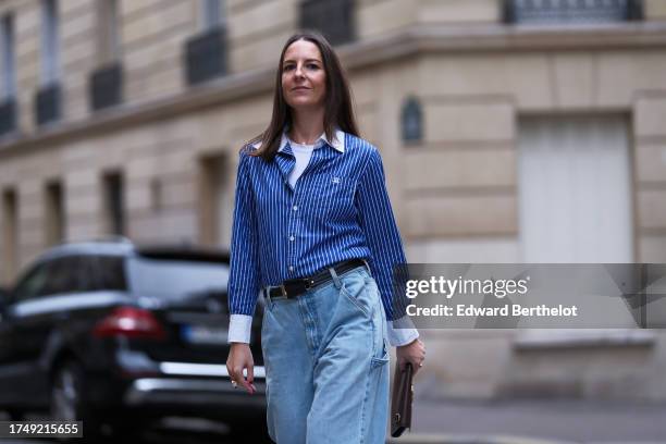 Alba Garavito Torre wears a blue and white striped shirt, a leather belt, blue flared denim jeans / pants, a brown leather clutch, during a street...