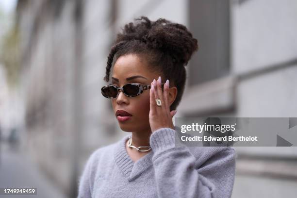 Ellie Delphine wears earrings, a necklace, sunglasses from LeSpeck, a mauve / pastel pale purple v-neck wool pullover from Rowen Rose, during a...