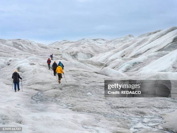 Tourists hiking on the ice. The brown sediment on the ice is created by the rapid melting of the ice. Landscape of the Greenland ice sheet near...