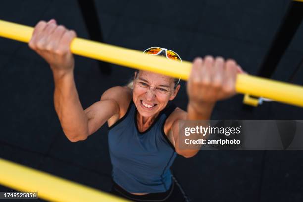athletische reife erwachsene frau, die anstrengende klimmzüge übt - work hard stock-fotos und bilder