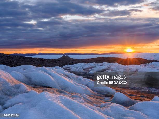 Midnight sun on the ice sheet. The brown sediment on the ice is created by the rapid melting of the ice. Landscape of the Greenland ice sheet near...