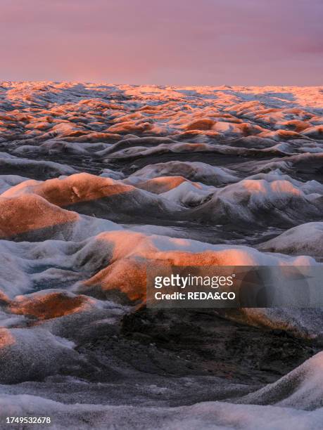 Midnight sun on the ice sheet. The brown sediment on the ice is created by the rapid melting of the ice. Landscape of the Greenland ice sheet near...