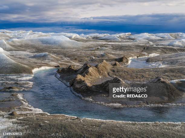 Drainage system with dirt cone on the surface of the ice sheet. The brown sediment on the ice is created by the rapid melting of the ice. Landscape...
