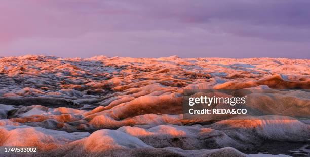 Midnight sun on the ice sheet. The brown sediment on the ice is created by the rapid melting of the ice. Landscape of the Greenland ice sheet near...
