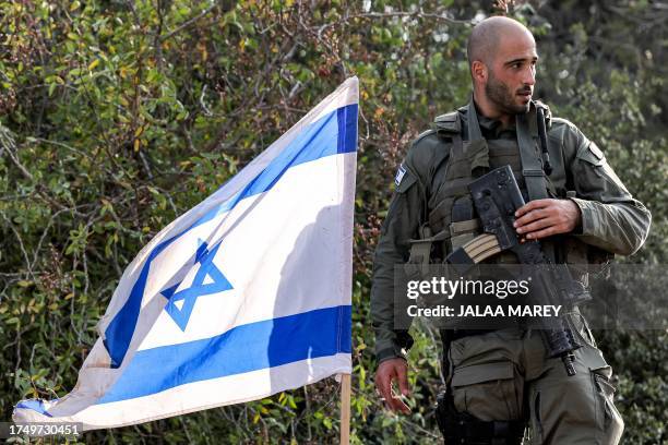 An Israeli army soldier stands with an assault rifle hanging across his chest by an Israeli flag at a position in the upper Galilee region of...