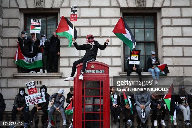 Protester waves Palestinian flags sitting on a red telephone box on Whitehall during the 'March For Palestine' in London on October 28 to call for a...