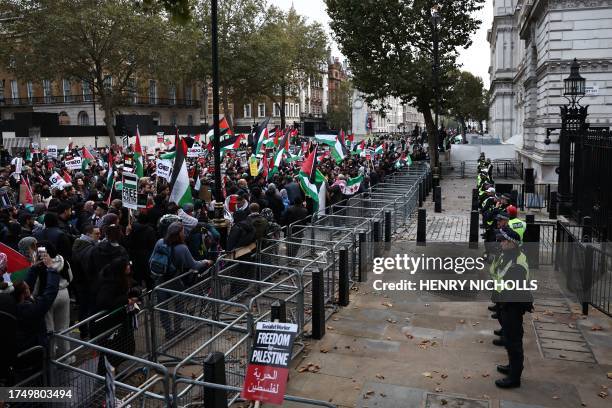 Police officers look on as protesters hold up placards and wave Palestinian flags at the gates of Downing Street after taking part in a 'March For...