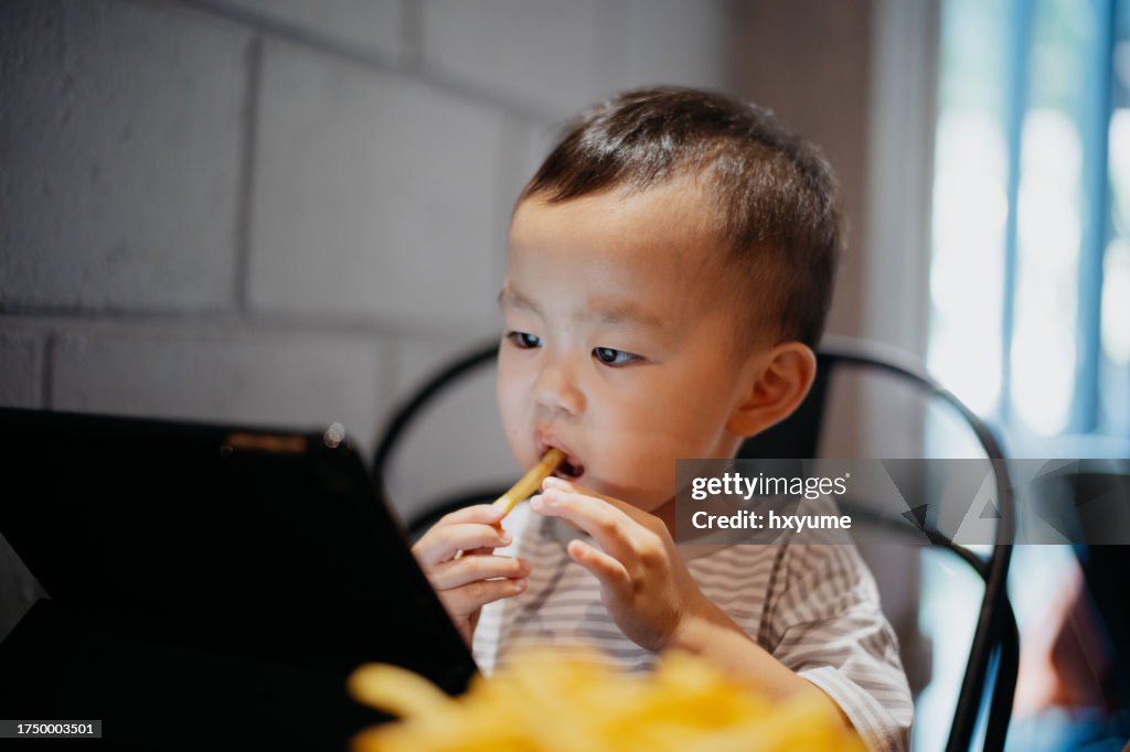 Young boy eating and playing digital tablet in cafe