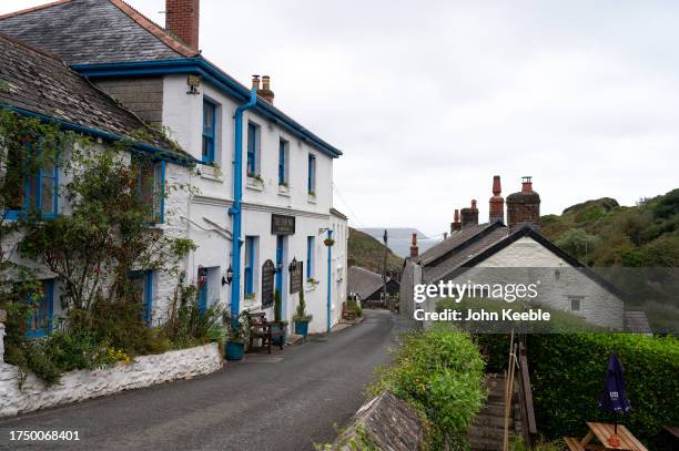 People walk along the street past the Ship Inn pub on an overcast wet day on September 17, 2023 in Portloe, England.