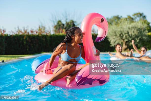 black woman enjoys a hot summer day in the pool with a giant inflatable flamingo - poolparty stockfoto's en -beelden