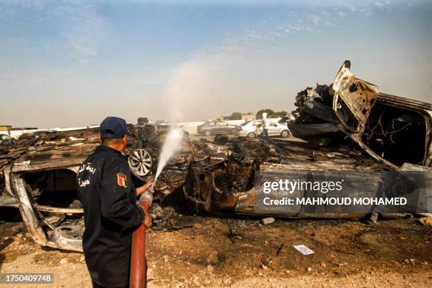 Civil defence members spray with water the wreckage of a burnt vehicle at the site of a large traffic collision along the Cairo-Alexandria desert...