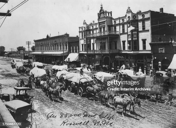 View of several horse-drawn wagons delivering a shipment of wool stopped in the middle of Main Street in front of the Grand Central Hotel in Roswell,...