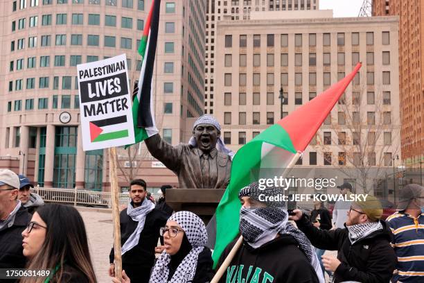 Protesters carrying a "Palestinians Lives Matter" sign walk past a statue of Martin Luther King Jr. Wearing a keffiyeh and holding a Palestinian flag...