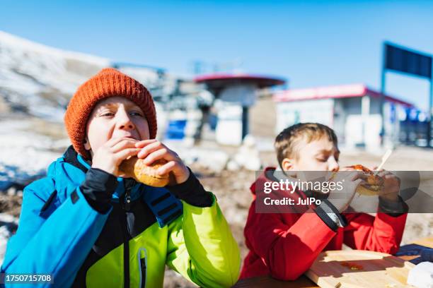 two boys eating burger after ski - winter sports family stock pictures, royalty-free photos & images