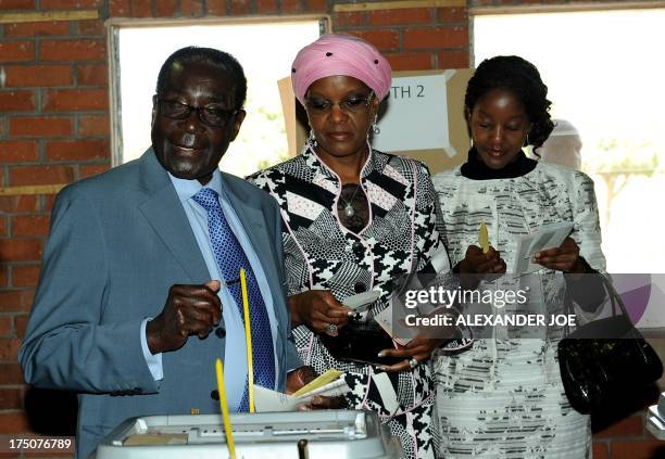 Zimbabwe President Robert Mugabe casts his vote by his wife Grace and daughter Bona at a polling booth in a school in Harare on July 31, 2013....