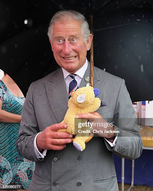Prince Charles, Prince of Wales is presented with a teddy bear for Prince George of Cambridge during a visit to the 132nd Sandringham Flower Show at...