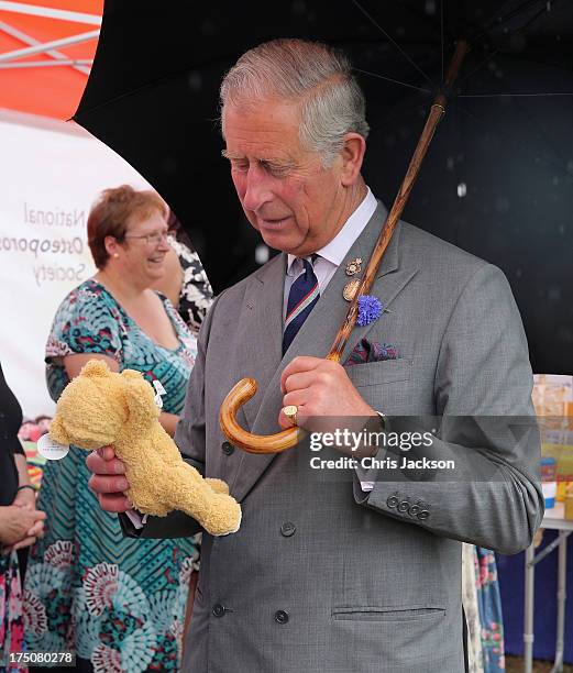 Prince Charles, Prince of Wales is presented with a teddy bear for Prince George of Cambridge during a visit to the 132nd Sandringham Flower Show at...