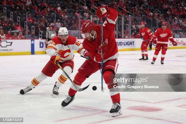 Compher of the Detroit Red Wings tries to control the puck in front of Adam Ruzicka of the Calgary Flames during the first period at Little Caesars...
