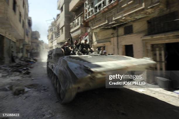 Soldiers of the Syrian government forces patrol on a tank in a devastated street on July 31, 2013 in the district of al-Khalidiyah in the central...