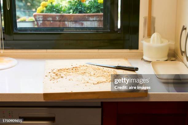 cutting board on kitchen counter with crumbs after cutting bread, window to the garden in the background. - breadcrumb stock pictures, royalty-free photos & images