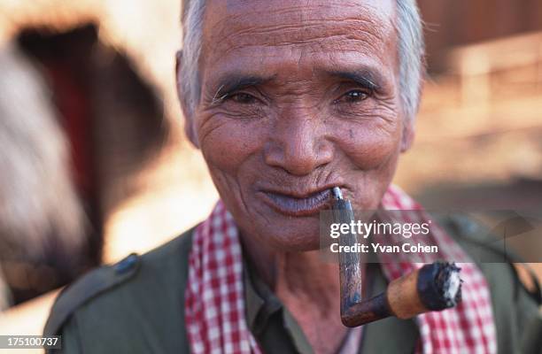 An elderly Phnong man smokes a pipe in the morning sunlight as he stands outside his hut in northeastern Cambodia..