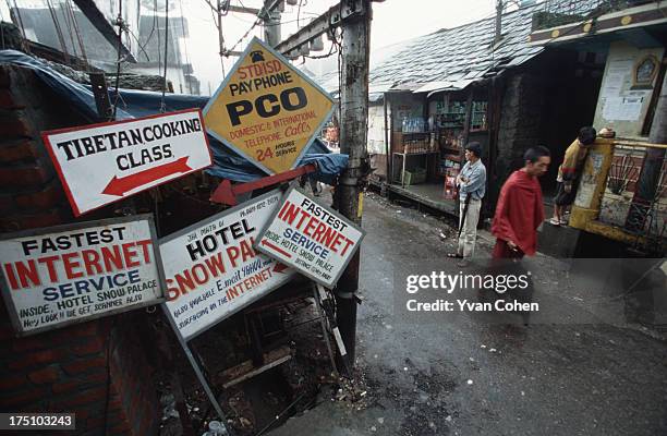 Tibetan monk walks past a jumble of signs for Tibetan cooking classes and internet cafes in the town of Dharamsala, in the foothills of the Indian...