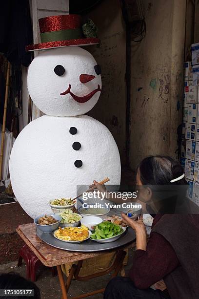 Woman enjoys a Vietnamese meal with a polystyrene snowman in the background. Christmas decorations are increasingly popular in Vietnam. .