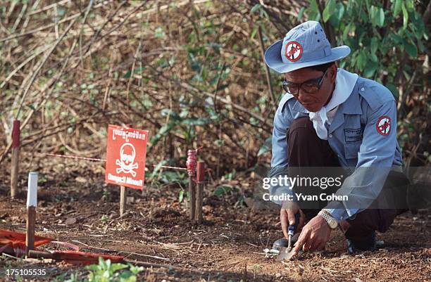 De-miner from the Cambodian Mine Action Center uses a trowel to gentle scrape the earth as he searches for mines. Beside him is a danger sign warning...