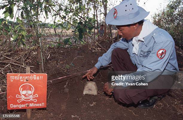 De-miner from the Cambodian Mine Action Center shows off an unexploded bomb with a danger sign beside it. Millions of anti-personnel mines still...