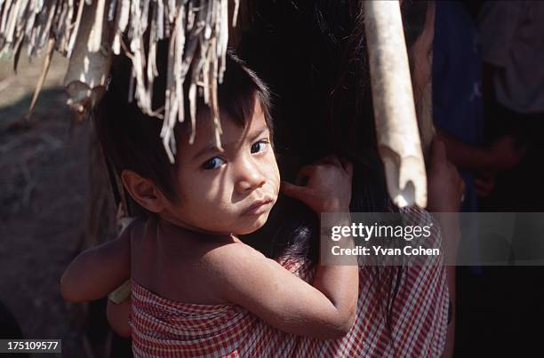 Hanging on the back of his mother supported by a Krama head scarf, a Cambodian child looks back nervously at the camera..