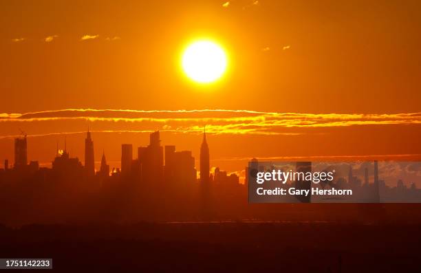 The sun rises behind the skyline of midtown Manhattan and the Empire State Building in New York City on October 22 as seen from West Orange, New...