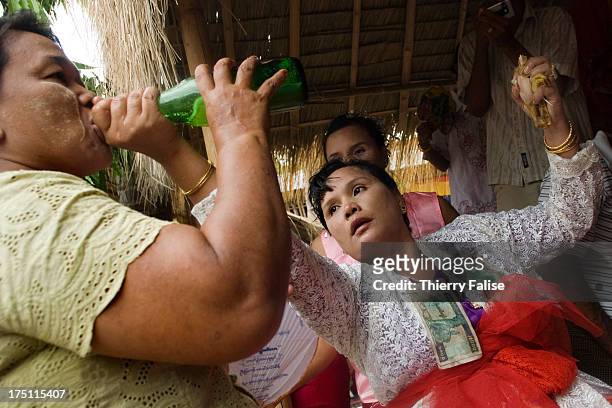 While holding a piece of chicken in a hand, a medium in trance pours beer into a woman's mouth in order to appease the nat possessing that woman....