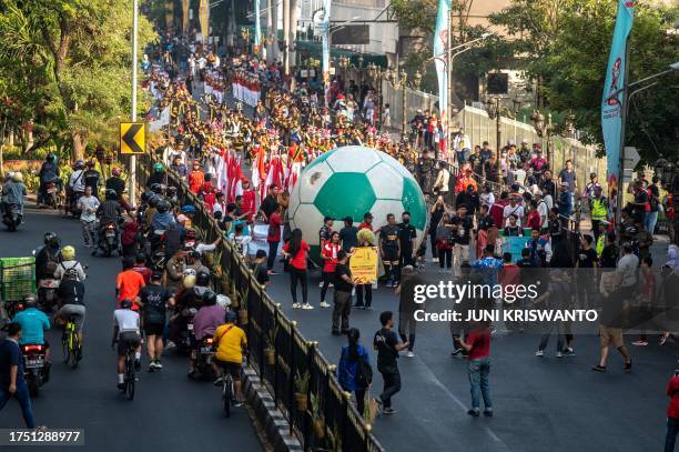 People crowd the street to watch a giant football being rolled out in a "Trophy Experience" event in Surabaya on October 29 ahead of the start of the...