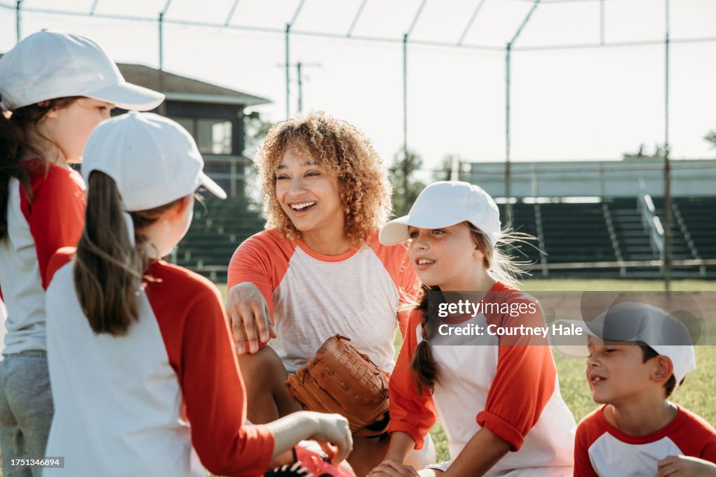 Co-ed Little League baseball features elementary-aged children as athletes, accompanied by coaches, on the ballfield
