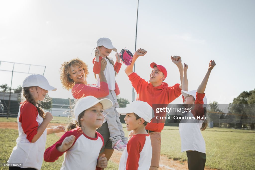 Celebration ensues as a team of Little League players, accompanied by their coaches, secures a baseball game win