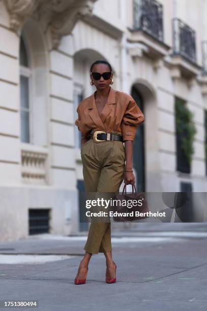 Emilie Joseph wears golden earrings, a vintage camel leather jacket worn as a top, high-waisted 7/8 paper bag pants; a black leather belt embellished...